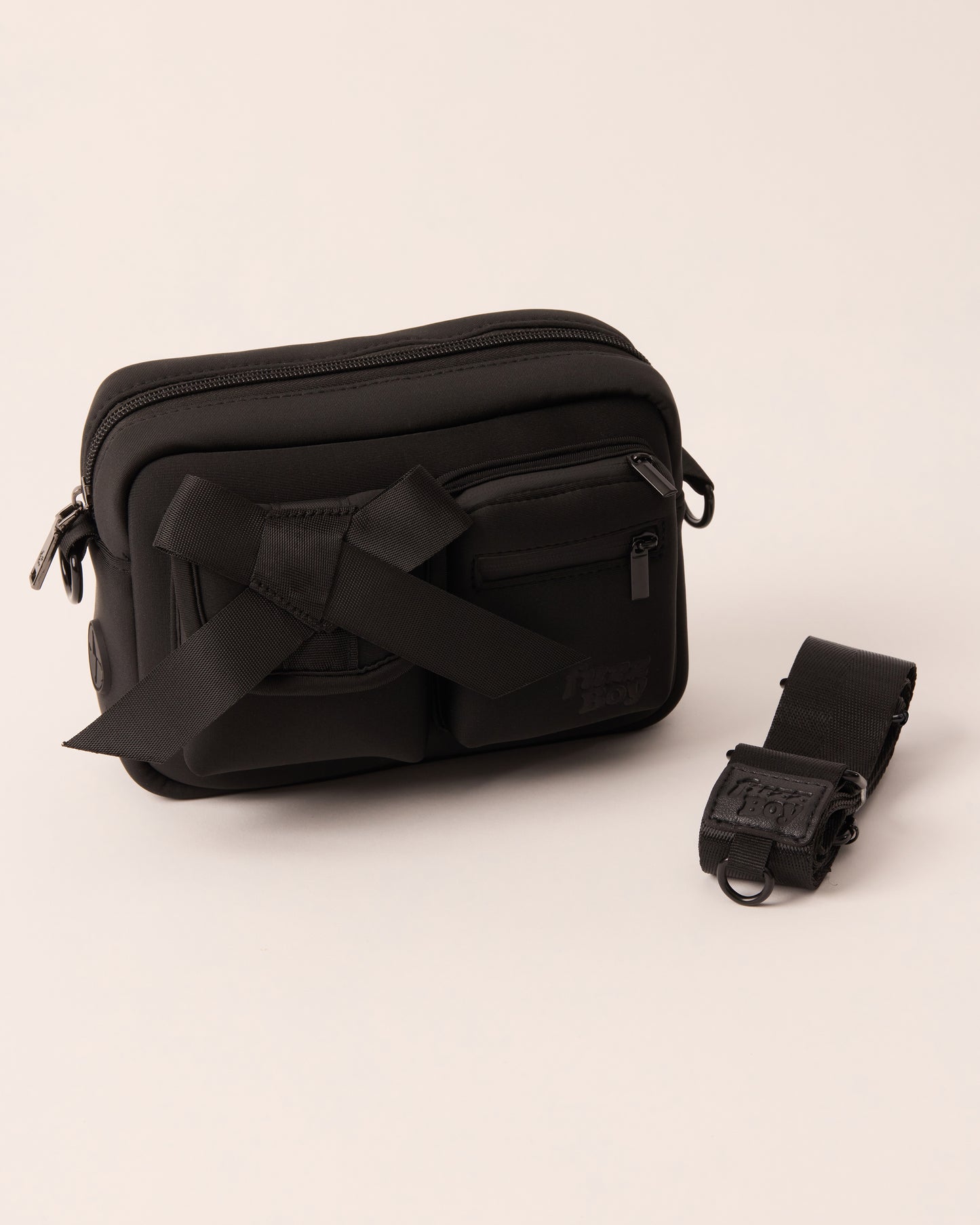 Black walking bag with a detachable strap. The bag features two front cargo pockets - on the left is a bow, and on the right are two zipper components.