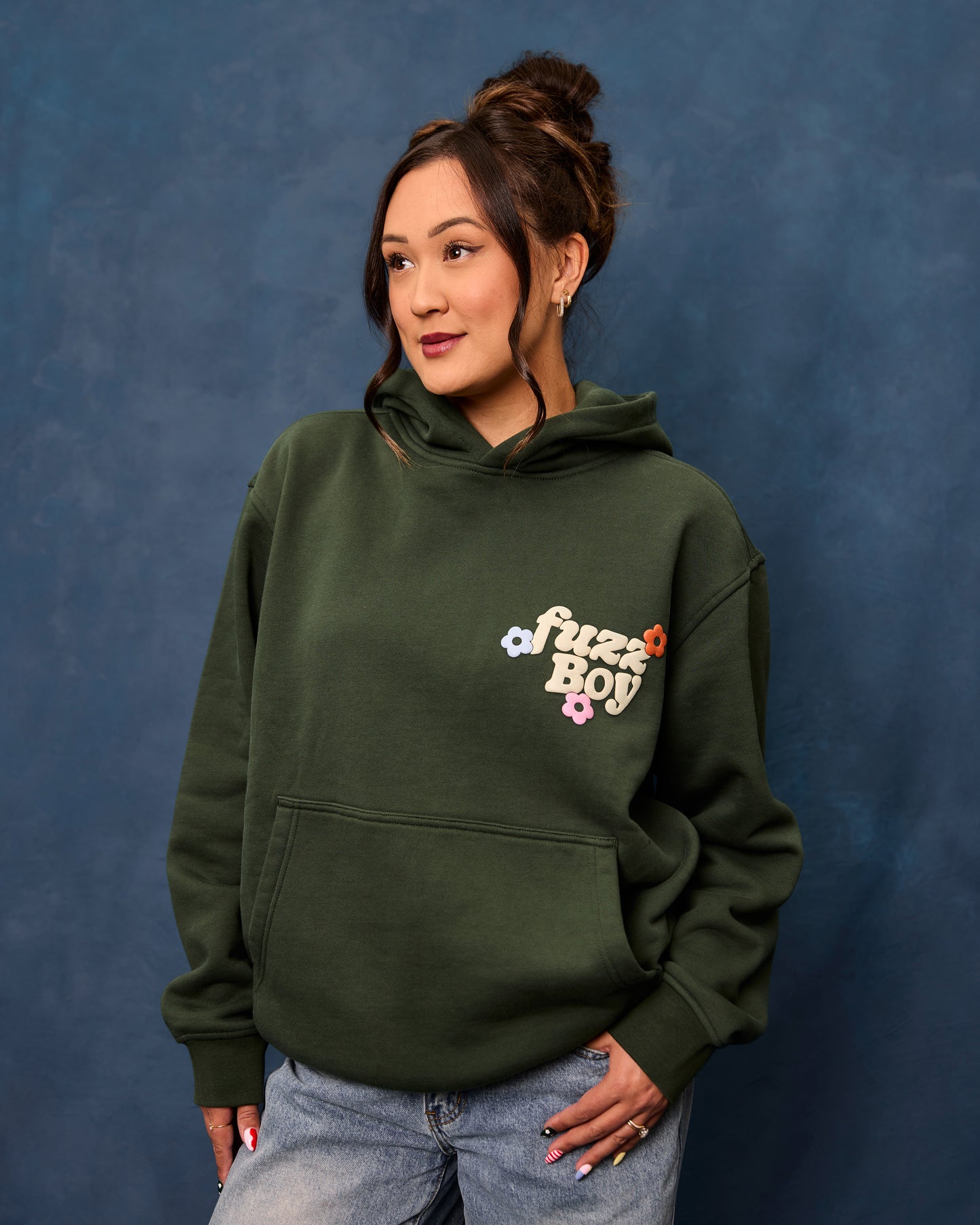 Woman wearing a forest green hoodie with 'Fuzzboy' logo.
