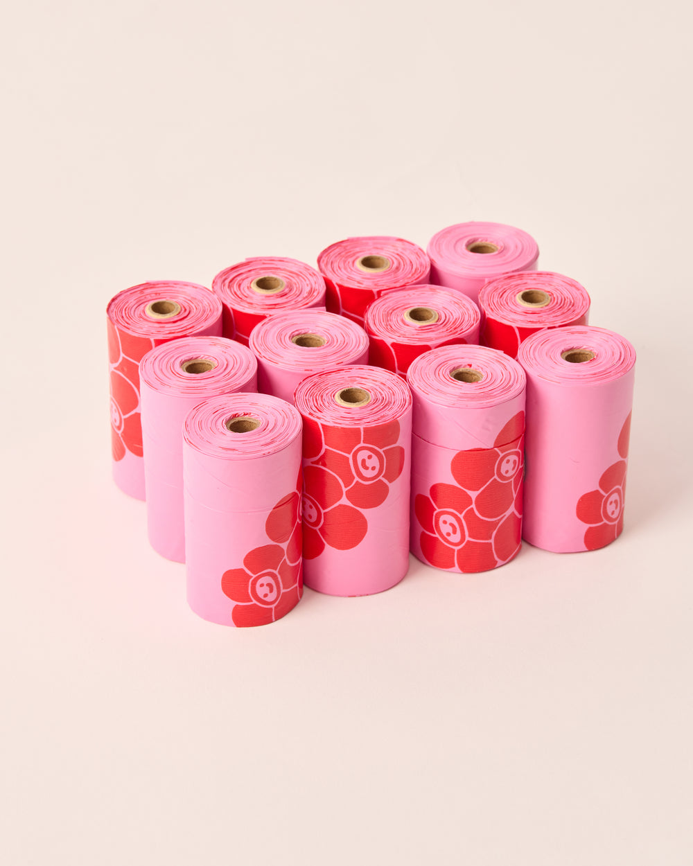12 rolls of pink poop bags with red graphics. Arranged neatly together.