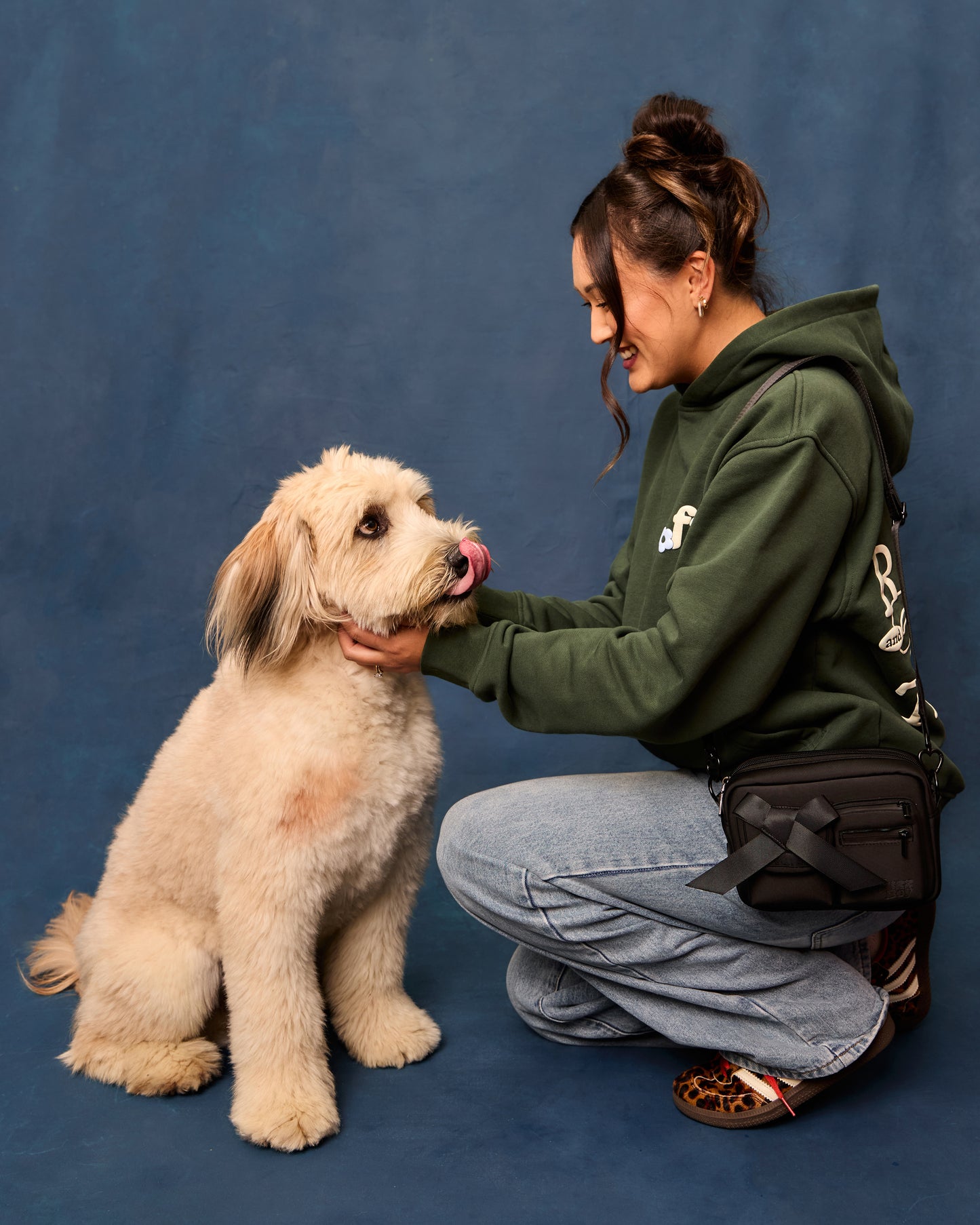 Woman in a green hoodie wearing the black walking bag on her shoulder, petting a dog.