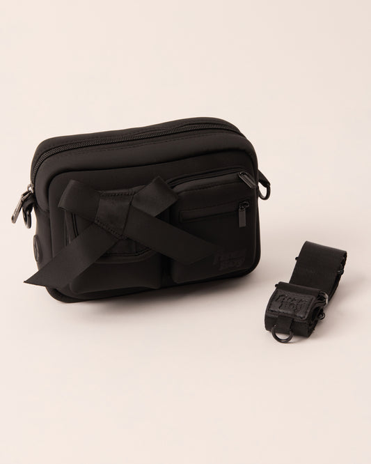 Black walking bag with a detachable strap. The bag features two front cargo pockets - on the left is a bow, and on the right are two zipper components.