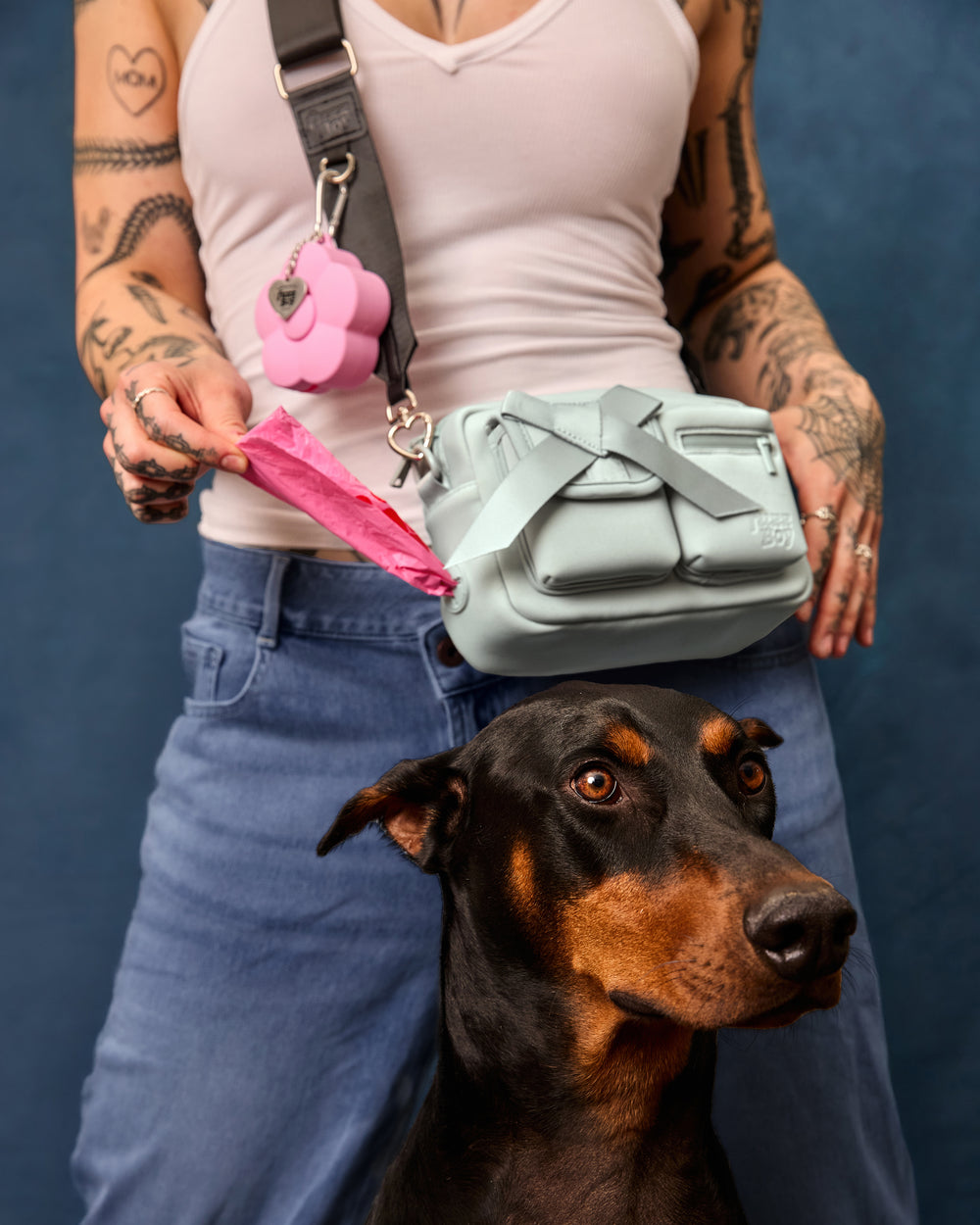 Woman pulls pink poop bag out of the built-in walking bag dispenser. A doberman is in the centre of the frame.