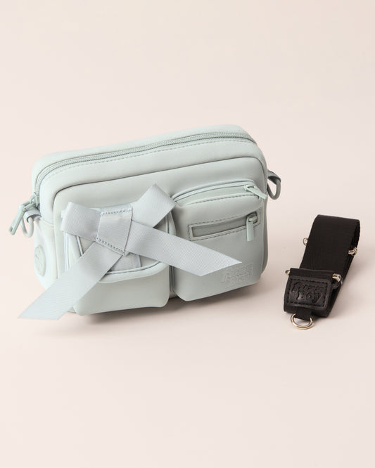 Light blue walking bag with a detachable strap. The bag features two front cargo pockets - on the left is a bow, and on the right are two zipper components.